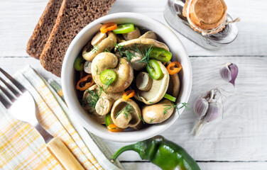 Pickled white mushrooms with peppers and herbs in a bowl on a white wooden table