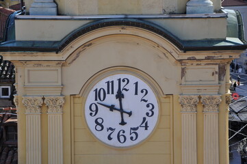 Fototapeta na wymiar White clock on the wall of the yellow city tower.