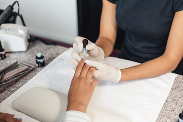 Obraz na płótnie Canvas Spa and beauty studio reopening after covid-19 epidemic. Hands of young woman client and african american master in rubber gloves paints nails with blue varnish