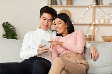Obraz premium Chinese Couple Using Smartphone Relaxing Sitting On Couch At Home