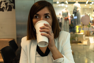 Close-up photo of an attractive young female that is wearing a white suit  and drinking coffee
