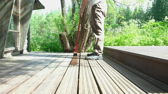 A Caucasian male, 45-50 years old, holds a paint brush in his hand. Painter paints a wooden terrace.