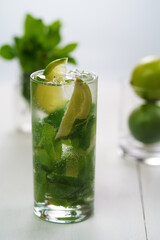 Fresh mint mojito served in high ball glass with fresh limes and mint in bokeh. White wooden table, high resolution