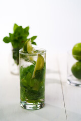 Fresh mint mojito served in high ball glass with fresh limes and mint in bokeh. White wooden table, high resolution
