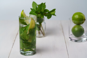 Fresh mint mojito served in high ball glass with fresh limes and mint in bokeh. White wooden table, high resolution