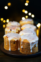 Traditional Easter kulich pastry served on dark brown plate. Wooden table, festive lights, high resolution