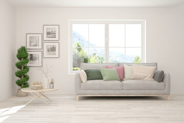 Fototapeta premium White living room with sofa and summer landscape in window. Scandinavian interior design. 3D illustration