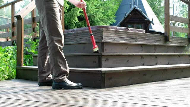 A Caucasian male, 45-50 years old, holds a paint brush in his hand. Painter paints a wooden terrace.