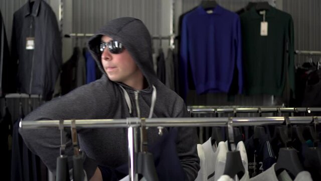 A man in a hood and glasses steals a T-shirt from a store. Clothing store.