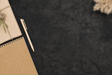 One gift wrapped in a craft paper and a twine. A notepad and a pen on black concrete background. Copy space, top view, flat lay.