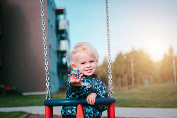 Young toddler boy swinging at children playground.