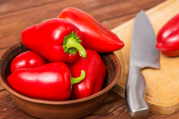 Fototapeta na wymiar Red sweet pepper in the plate on the table with wooden chopping board and knife. Fresh food. Healthy lifestyle