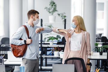 Modern greeting with colleague during coronavirus outbreak. Millennial guy and lady in protective masks came to work in morning and touch with elbows to say hello