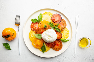Delicious caprese salad with ripe colorful tomatoes and mozzarella cheese with fresh basil leaves. Italian food, top view