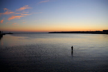 Fototapeta premium Fisherman at sunset. Man fishing in shallow water near the shore in a calm evening. Silivri, Turkey