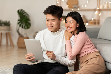Happy Korean Couple Using Tablet Computer Sitting At Home
