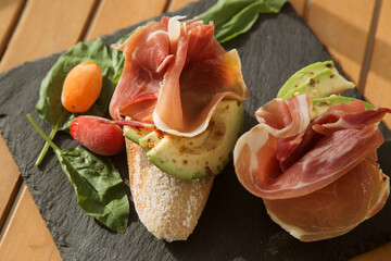 bruschetta with ham (bacon) and avocado on a black plate. The option of a beautiful and healthy Breakfast or snack