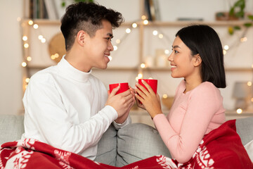 Korean Couple Having Coffee Celebrating Xmas Sitting On Couch Indoors