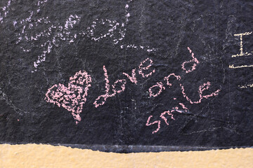 Love and smile handwriting on a chalkboard with heart drawing next to the text.