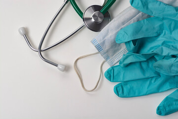 Stethoscope, medical mask and gloves on a white table.