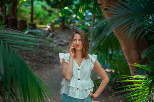 Mujer joven habla por el movil en un parque con palmeras