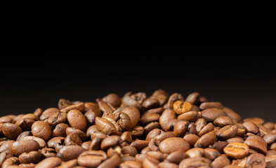 Roasted coffee beans on black background. Heap of coffee beans. Poured coffee close-up