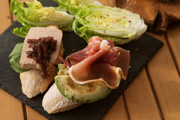 bruschetta with liver pate and onion jam and bruschetta with bacon and avocado on a black plate and wooden table