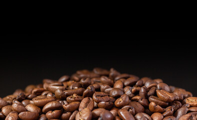 Coffee beans on a black background. Heap of coffee beans. Poured coffee close-up