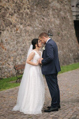 Happy newlyweds walking in the old castle and hug each other. Beautiful young bride and attractive groom in front of stone wall