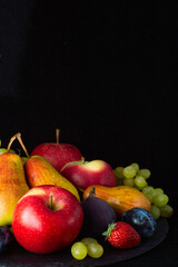 Still life of fruits, apples, pears, grapes, figs, strawberries and plums on a black background.