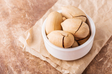 Pecans in shell in white bowl on craft paper, brown background, top view,healthy content