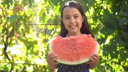 Happy child eating watermelon. Kid eat fruit outdoors. Little girl playing in the garden biting a slice of watermelon.
