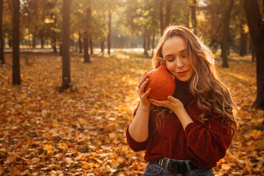 Young beautiful smiling woman with long curly hair holding orange halloween pumpkin on autumn park yellow trees background. Fall autumn halloween concept.