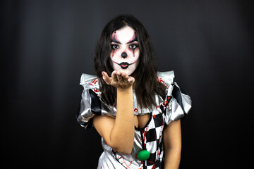 woman in a halloween clown costume over isolated black background looking at the camera blowing a...