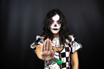 woman in a halloween clown costume over isolated black background serious and doing stop sing with palm of the hand.