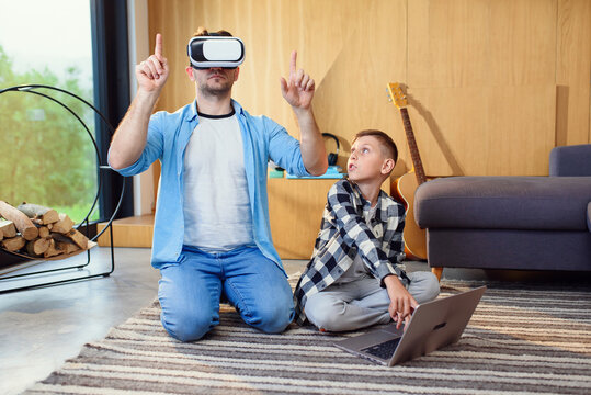 Happy father and son in virtual reality headsets playing with gamepads at home. Augmented reality concept.