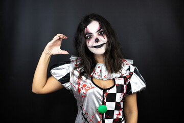 woman in a halloween clown costume over isolated black background smiling and confident gesturing with hand doing small size sign with fingers looking and the camera. Measure concept.