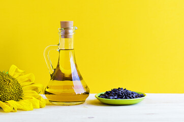 sunflower oil with flower and seeds in a glass jug on yellow and wooden background, copy space, place for text. natural healthy food concept