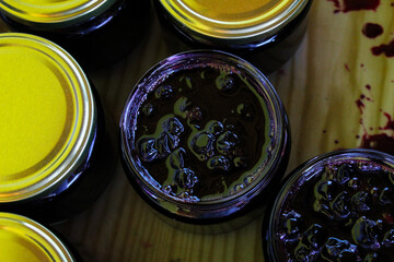 Full jars of homemade chokeberry jam on a tray. Some jars already closed, others ready to close. Aronia.