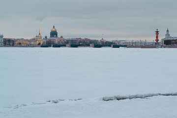 Winter embankment of Saint Petersburg with colored buildings and St. Isaac's Cathedral on banks of frozen Neva river in white snow with bridge. Light day