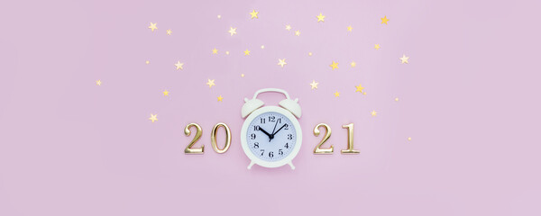 Numbers 2021 and alarm clock are decorated with star confetti on pink background. Minimal concept of Christmas and New Year. Top view, banner