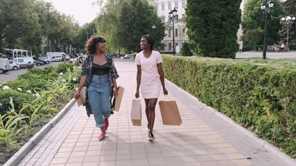 Two afro american women friends in the city. Friends on a shopping trip carrying colorful shopping bags.