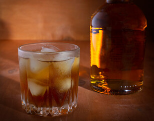 misted glass of whiskey with ice on a wooden background in the distance bottle with whiskey
