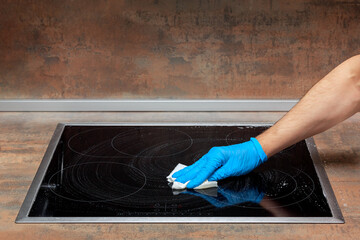 Adult man removes the remaining detergent from the kitchen electric stove with a paper towel