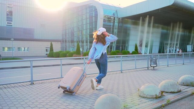 Young stylish girl hipster tourist runs a suitcase is late for departure to the airport or bus station train in the city urban background. woman traveling student running hurried down street