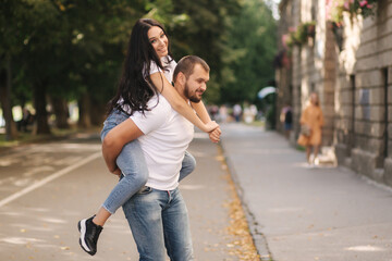 Beautiful gilr climbed on her boyfriend back and hug him. Happy smiled couple spend time in city