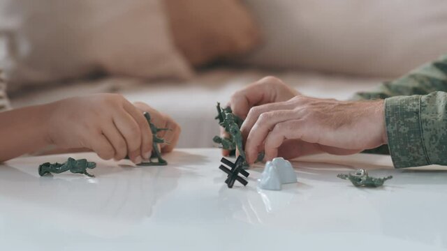 Close up shot of unrecognizable boy and his father in uniform playing with toy soldiers on table