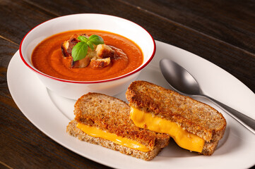 Bowl of tomato soup and grilled cheese sandwich on a dark wooden surface with copy space