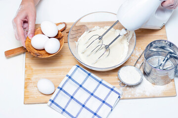 making dough for bread or homemade baked goods. ingredients on the desk. female hands hold a mixer for mixing dough