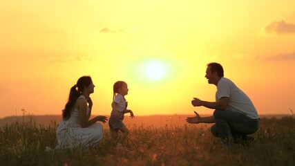 Fototapeta na wymiar little daughter goes from mom to dad, hugs and kisses her parents in rays of warm sun. Happy family walks in park at sunset. Mom, dad and baby. healthy family plays in field. Happy family concept